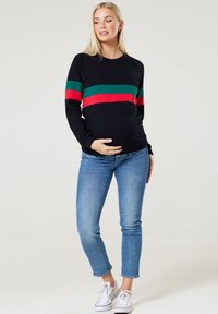 Schwarzes Langarm-Sweatshirt mit grünen und roten horizontalen Streifen, kombiniert mit hellblauen Skinny-Jeans und weißen Sneakers.