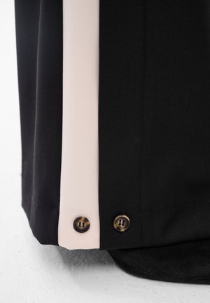 Close-up van zwarte en beige stoffenpanelen met twee kleine schildpadknopen langs de naad op een vlak oppervlak.