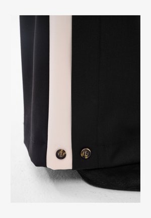 Zbliżenie czarnych i beżowych paneli materiałowych z dwoma małymi guzikami w kolorze żółwia przy szwie na płaskiej powierzchni.