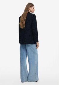 Svart blazer med ett präglat mönster och skräddarsydd passform, kombinerad med högmidjade, vida ljusblå jeans i denimmaterial.