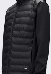 Gilet imbottito nero con design trapuntato, chiusura a zip e tessuto morbido sui lati. Presenta una piccola etichetta con il logo nella parte inferiore.