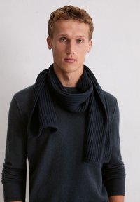 Donker marineblauwe geribbelde wollen sjaal losjes om de nek gedragen, gecombineerd met een bijpassende donkere trui met ronde hals en lange mouwen.