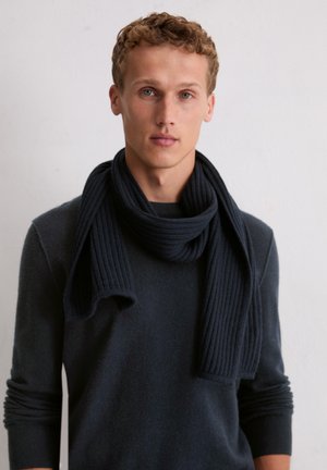 Écharpe en laine côtelée bleu marine foncé, portée lâchement autour du cou, associée à un pull assorti de couleur foncée, avec un col rond et des manches longues.