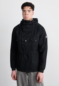 Sort pullover-jakke med høj krave, justerbar hætte, lommer foran og snor i taljen. Fremstillet af et let, tekstureret stof.
