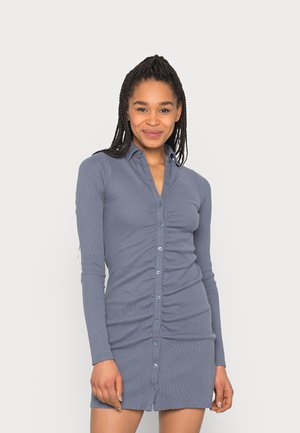 Vestido de manga longa, com botões, em azul suave, apresentando uma textura arrebitada e detalhe franzido à frente, terminando acima dos joelhos.