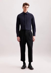 Granatowa krótkia koszula zapinana na guziki, o dopasowanym kroju, z długimi rękawami, zestawiona z czarnymi plisowanymi spodniami i czarnymi skórzanymi butami. Gładka faktura tkaniny.