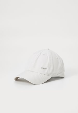 Casquette de baseball blanche avec un petit logo en métal de swoosh Nike à l'avant, affichée sur un fond blanc uni.