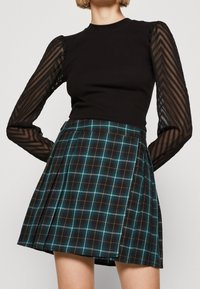 Top nero con maniche a sbuffo trasparenti e testurizzate, abbinato a una gonna a quadri in nero, teal e giallo con pieghe e una vita strutturata.