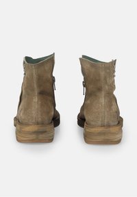 Bottines en daim marron avec un bout arrondi, un talon en bois empilé et des coutures apparentes. Elles présentent une doublure en tissu vert et une fermeture éclair.