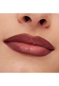 Läppstift i en djup mauve nyans på fylliga läppar, med en mjuk textur och subtil lyster, mot en ljus hudbakgrund.