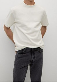 Maglietta bianca a maniche corte con collo a giro, realizzata in tessuto morbido, abbinata a jeans in denim grigio scuro con vestibilità classica e una leggera texture.
