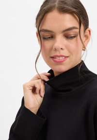 Czarny sweter z golfem z prążkowanym kołnierzem i mankietami, wykonany z miękkiej, teksturowanej tkaniny. Model delikatnie poprawia kołnierz.