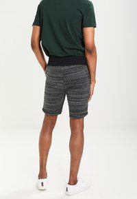 Shorts gris texturé avec une taille élastique noire, offrant une coupe décontractée, associés à une chemise verte et des baskets blanches.
