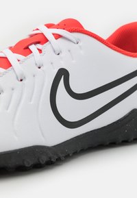 Nike soccer shoes featuring a white synthetic upper, black logo, red accents on the collar and lace area, and textured black outsole.