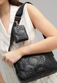 Borsa a spalla nera trapuntata con motivo floreale in rilievo, cinturino regolabile e pochette con zip staccabile. Accenti in hardware dorato.