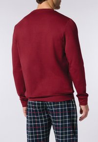Maglione burgundy con collo a giro e maniche lunghe, abbinato a pantaloni da pigiama a scacchi nei toni del blu, verde e rosso, visibili in vita.
