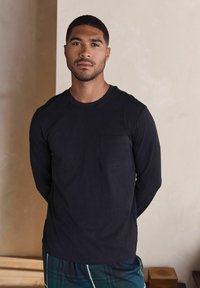 Pitkähihaiset mustat paita, jossa on pyöreä pääntie ja rintatasku, yhdistetty ruutukuosisiin pyjamahousuihin. Sileä pinta, rento istuvuus.