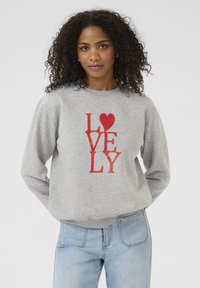 Grauer Pullover mit rotem Druck, auf dem das Wort "LIEBE" vertikal angeordnet ist, ergänzt durch ein Herz-Symbol, gefertigt aus weichem, strukturiertem Stoff.