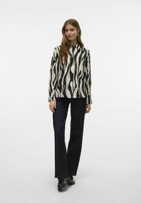 Zwart-wit gestreepte blouse met lange mouwen, met knopen aan de voorkant, in combinatie met donkerblauwe rechte spijkerbroek en zwarte schoenen.