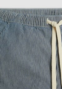 Tessuto a righe blu e bianco, con una vita elastica e un cordino color crema. Materiale leggero con una texture liscia.