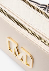 Borsa beige con superficie testurizzata, cerniera dorata e un logo dorato prominente. Presenta linee pulite e un design strutturato.