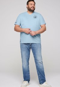 Camiseta de algodón de color azul claro con escote en V que presenta un diseño impreso en el pecho y mangas cortas. Combinada con jeans de color azul claro y zapatillas blancas.