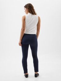 White sleeveless top and navy fitted pants. Top has a high neckline, and pants feature a slim cut with back pockets. Black flat shoes visible.