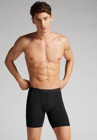 Černé boxerky s přiléhavým střihem a měkkou texturou. Mají kontrastní elastický pas s logem a délku do poloviny stehna.