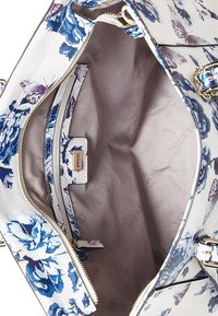 Käsilaukku, jossa on kukka- ja perhoskuvio, vaaleanbeige kangasvuori, vetoketjullinen tasku ja kultasävyiset yksityiskohdat. Brändi "Guess" näkyy sisäpuolella.