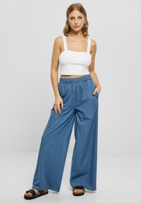 Leichtes, weißes bauchfreies Oberteil mit breiten Trägern, kombiniert mit weiten, blauen Denim-Hosen mit elastischem Bund und seitlichen Taschen.