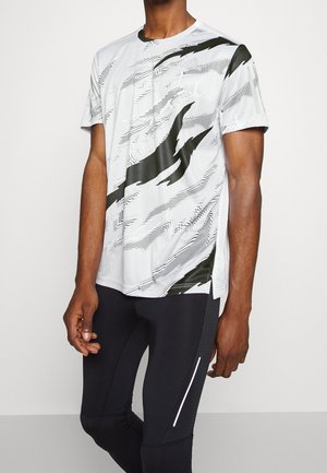 Mand iført en hvid og sort mønstret kortærmet træningsshirt og sorte tætsiddende træningsbukser med en refleksstribe.