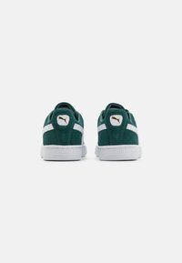 Sneaker in suede verde con accenti bianchi, dotati di suola in gomma testurizzata e un logo dorato sul tallone. La vista posteriore mette in mostra un colletto imbottito.