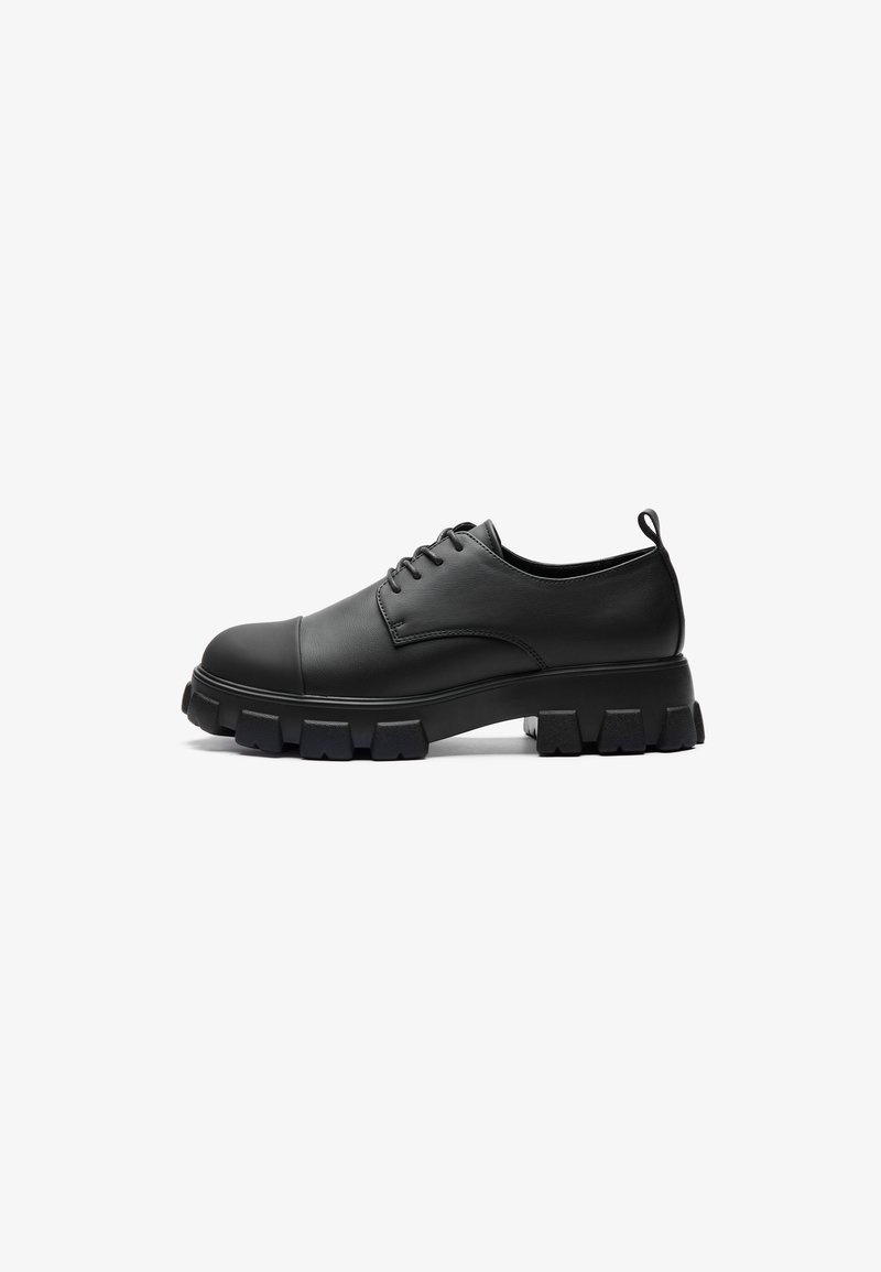 Chaussure en cuir noir avec bout rond, design à lacets, semelle épaisse et texturée, et languette au talon. Finition lisse avec un surpiquage minimaliste.