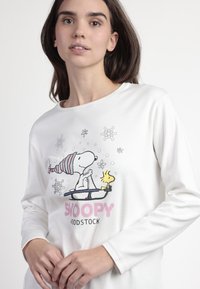 Camiseta de manga larga blanca con gráficos de Snoopy y Woodstock en colores pastel, con un escote redondeado y un corte relajado.