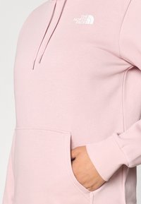 Világos rózsaszín kapucnis pulóver elején zsebbel, bordázott mandzsettákkal és húzózsinórokkal. Bal mellrészen fehér logóval. Puha anyagtextúra.