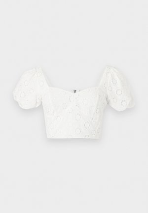 Blouse blanche courte avec manches courtes bouffantes et broderie œillet florale, avec un col carré et une fermeture éclair au dos.