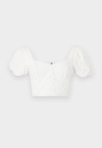 Blouse blanche courte avec manches courtes bouffantes et broderie œillet florale, avec un col carré et une fermeture éclair au dos.