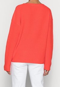 Pull en maille corail à coupe ample, manches longues larges et texture côtelée. Associé à un pantalon blanc à coupe droite.