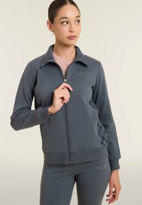 Giacca grigia con zip, colletto, pannelli laterali testurizzati e un logo sobrio. Presenta polsini e orlo a coste per un look aderente.
