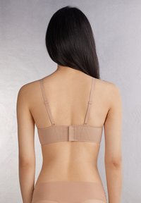 Beige bh met verstelbare bandjes, een glad achterpaneel en een haak-en-oogsluiting. Het materiaal lijkt zacht met minimale stikseldetails.