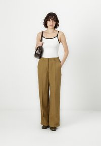 Pantalones de tiro alto en marrón con corte ancho y una textura suave. Combinados con una camiseta sin mangas blanca con ribete negro. Bolso de hombro marrón.