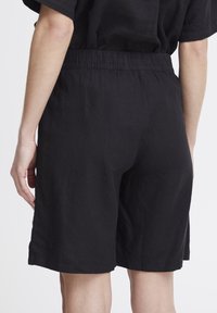 Shorts en lin noir avec une taille élastique, une coupe décontractée, une longueur mi-genoux et des fentes sur les côtés pour faciliter les mouvements.