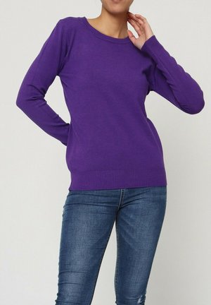 Pull en maille violet à manches longues, col rond, avec un ourlet et des poignets côtelés ; associé à un jean bleu, mettant en valeur une coupe ajustée.