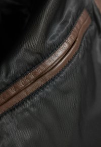 Fekete nylon táska belseje barna bőrkiegészítővel. Texturált felülettel rendelkezik, és sima él van a varrás mentén.