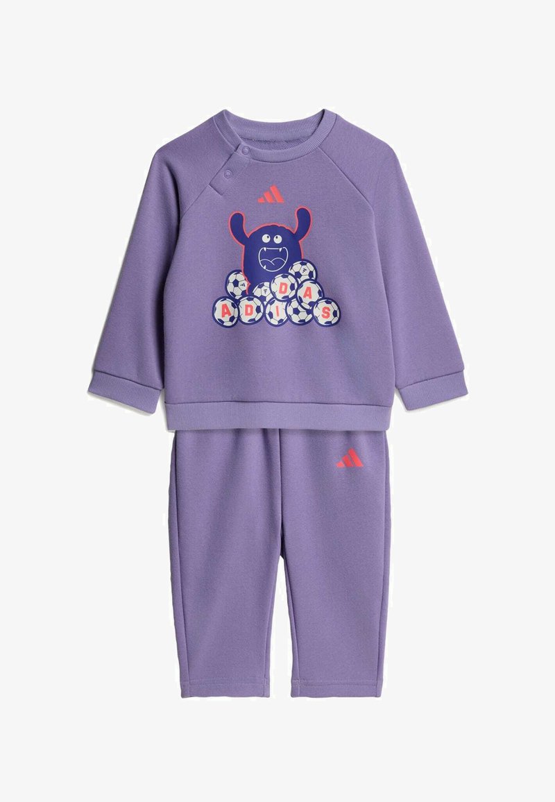 Ensemble violet pour tout-petit composé d'un sweat-shirt et d'un pantalon avec un motif monstre ludique et des ballons de football formant "ADIDAS", avec un logo Adidas rouge sur les deux pièces.