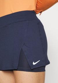 Skort deportivo en color navy con una cinturilla ancha, aberturas laterales y un logo blanco de Nike en la parte inferior izquierda; confeccionado con una tela elástica y suave.