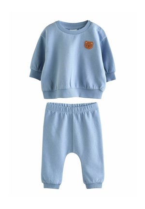 Hellblaues Sweatshirt- und Hosen-Set. Das Sweatshirt hat kurze Ärmel und ein Bären-Patch. Die Hose hat einen elastischen Bund und schmal zulaufende Bündchen.
