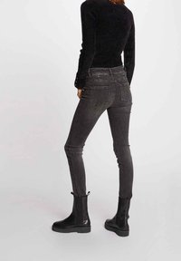 Schwarze, hoch taillierte Skinny-Jeans mit verblasster Textur, Knopfdetails und zwei Gesäßtaschen, kombiniert mit schwarzen Stiefeletten.