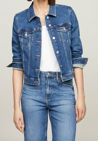 Jeansjacka i medelblått, med bröstfickor, silverknappar och uppvikta ärmar. Kombinerad med ljusblå högmidjade jeans.