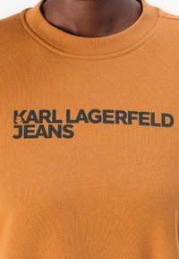 Bruine geribde t-shirt met opvallende zwarte tekst "KARL LAGERFELD JEANS" op de voorkant, met een klassieke ronde hals.
